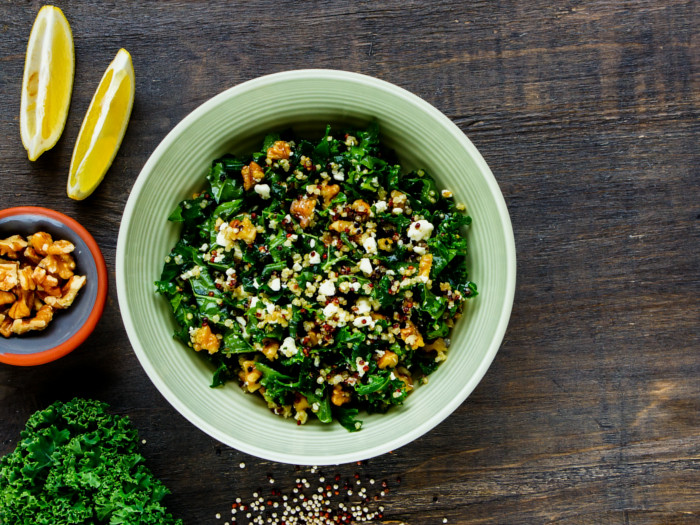 Kale and quinoa salad in a bowl on a brown table top with lemon, broccoli, and walnuts
