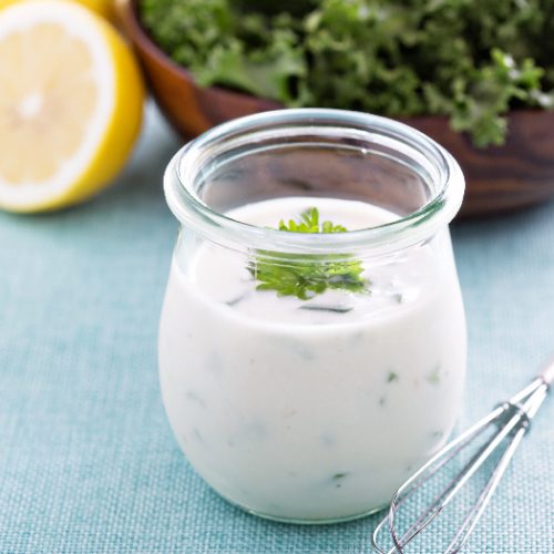 ranch dressing in a glass bottle next to a green salad with a lime half