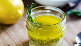 Close up of a keto salad dressing made with olive oil, fresh lemon juice, and herbs like rosemary
