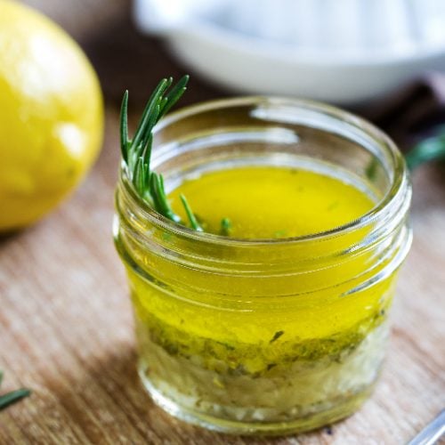 Close up of a keto salad dressing made with olive oil, fresh lemon juice, and herbs like rosemary