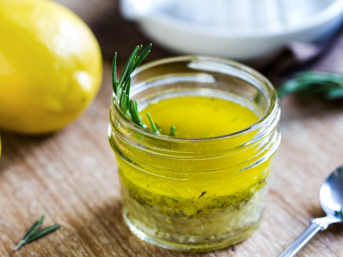 Close up of a keto salad dressing made with olive oil, fresh lemon juice, and herbs like rosemary