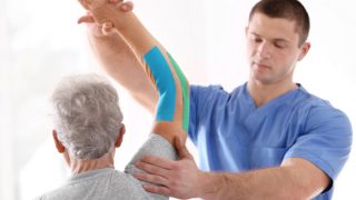 An older man with kinesio tape on his arm getting a kinesio taping therapy  by another man