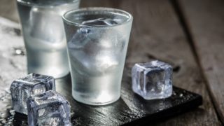 Two small glasses filled with kirsch and some ice on a wooden table-top
