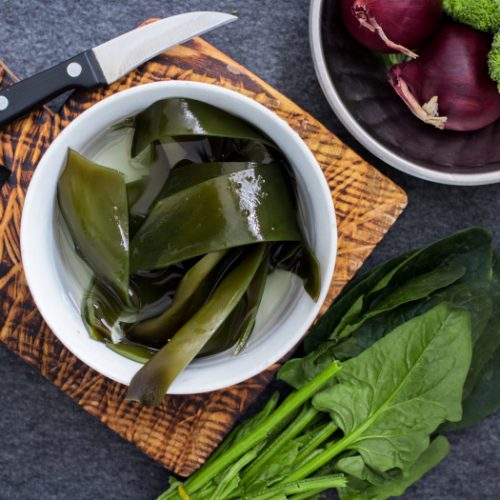 Wet soaked kombu seaweed leaves in a bowl with other fresh vegetables