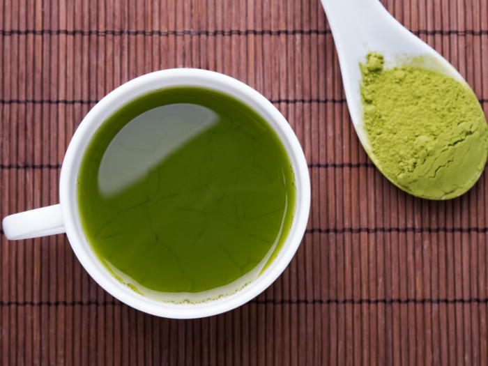 A cup full of tea accompanied by a spoonful of kratom powder