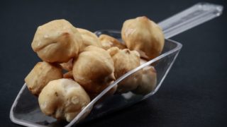 Close-up of a transparent scoop filled with kukui nuts on a dark background