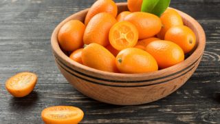 A bowl of whole and halved kumquats on a dark table