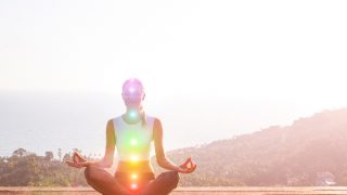 A woman in a half lotus pose practicing meditation with all seven chakras glowing