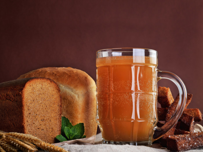 A beer glass filled with kvass, with rye bread and dried ryegrass in the background