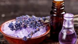Two bottles with lavender oil and a bowl of sea salt with lavender flowers on a wooden table