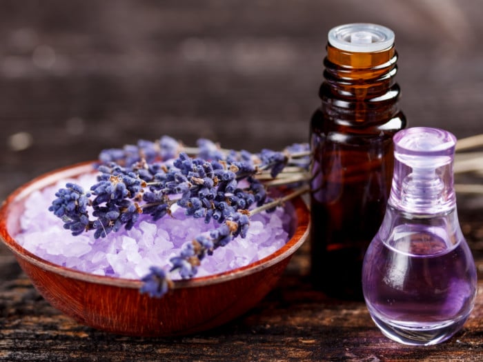 Two bottles with lavender oil and a bowl of sea salt with lavender flowers on a wooden table