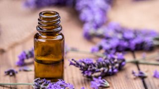 A glass bottle of lavender essential oil kept next to lavender sprigs on a wooden table