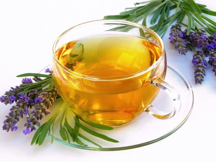 A cup of lavender tea with flowers and leaves on a white background