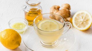 A cup of lemon ginger tea with fresh lemon and ginger on a white wooden table