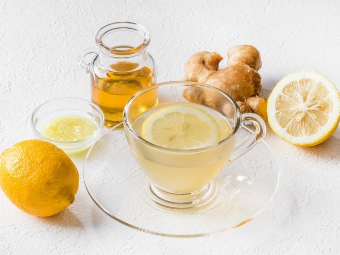 A cup of lemon ginger tea with fresh lemon and ginger on a white wooden table