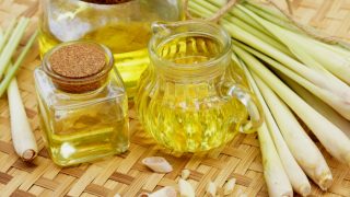 3 jars of lemongrass oil with whole and sliced lemongrass on a mat