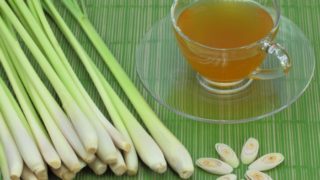A cup of lemongrass tea with fresh lemongrass on a green background