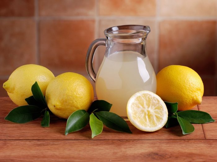 Glass jar filled with lemon juice with lemons and lemon leaf on a wooden table