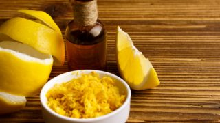 A bottle containing oil extracted from the peel of fresh lemons kept atop a wooden table