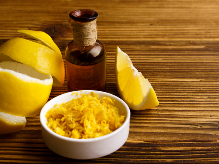 A bottle containing oil extracted from the peel of fresh lemons kept atop a wooden table