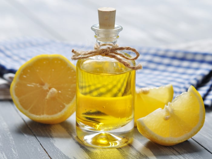 A bottle containing lemon oil kept next to sliced lemons atop a wooden table