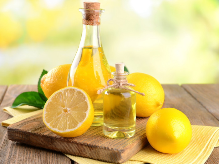 A bottle of lemon oil kept next to lemons, on a wooden table