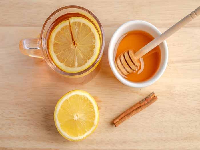 Lemon tea in a cup next to fresh lemon, honey, and cinnamon