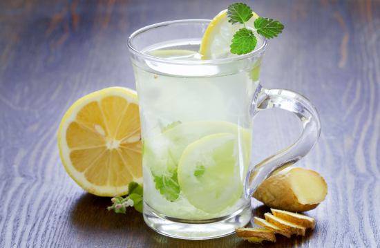 A glass of lemon water with slices of lemon, ice cubes, and mint in it.