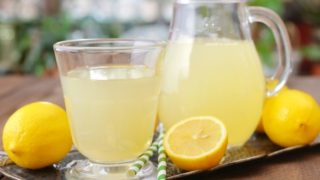 Close-up of a glass of lemon juice, lemon halves with a pitcher of lemon juice at the back.