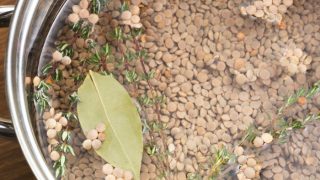Lentils, thyme, and bay leaf in a pot with water, ready for cooking.