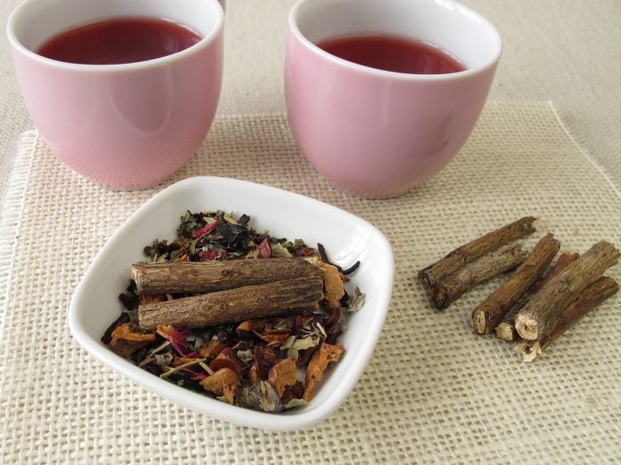 2 cups of licorice root tea and a white bowl of dried licorice roots on a mat