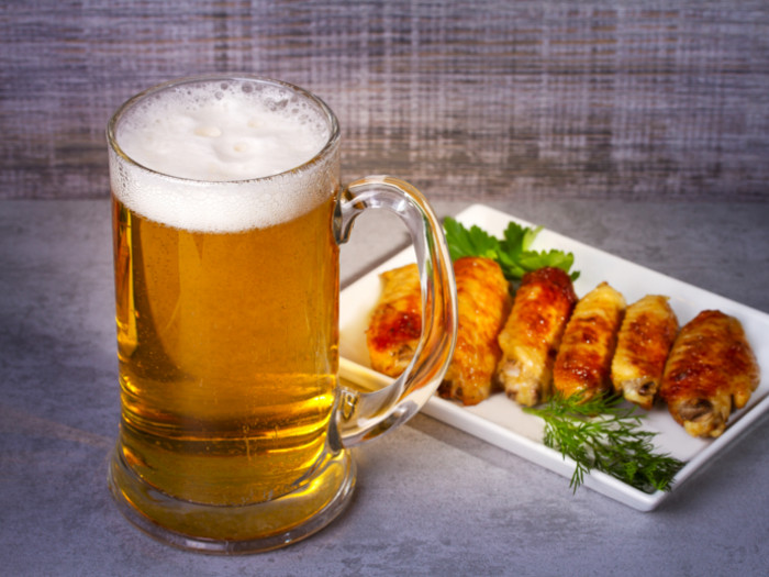 A mug full of beer with chicken wings in a plate next to it