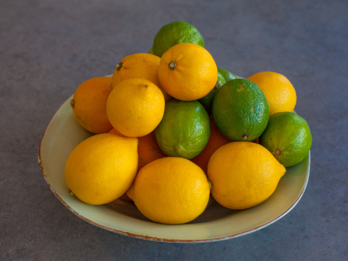 A bowl of lime and lemons on a grey background