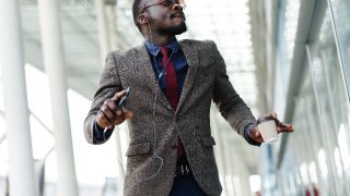 Young man in a suit listening seeming happy listening to music while carrying a coffee cup