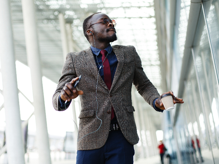 Young man in a suit listening seeming happy listening to music while carrying a coffee cup