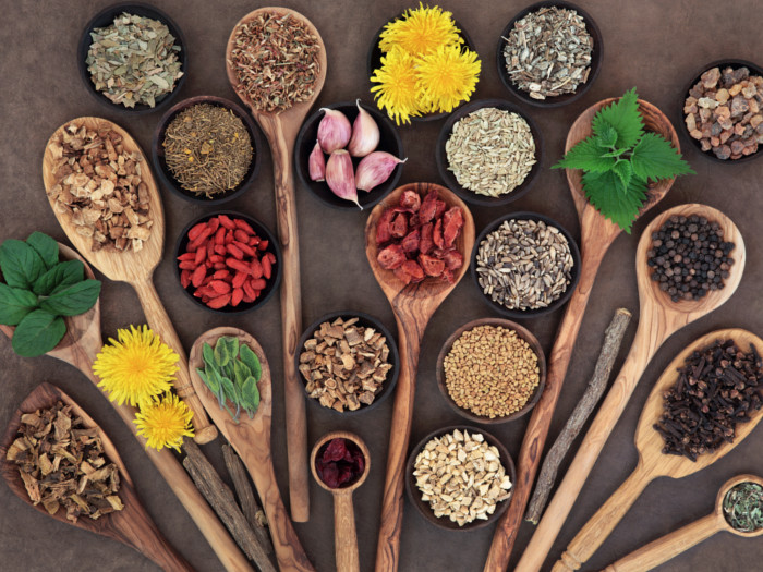 Various spoons containing different herbs and spices on a black background