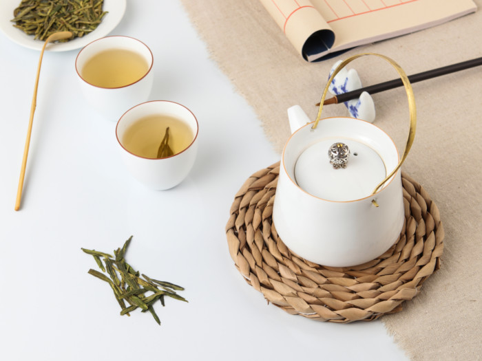 two small cups filled with longjing tea kept next to a tea kettle on a white table