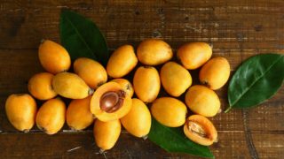 Close up of whole and halved loquats with leaves on a wooden table