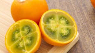 A half-sliced lulo with a full lulo on a wooden cutting board