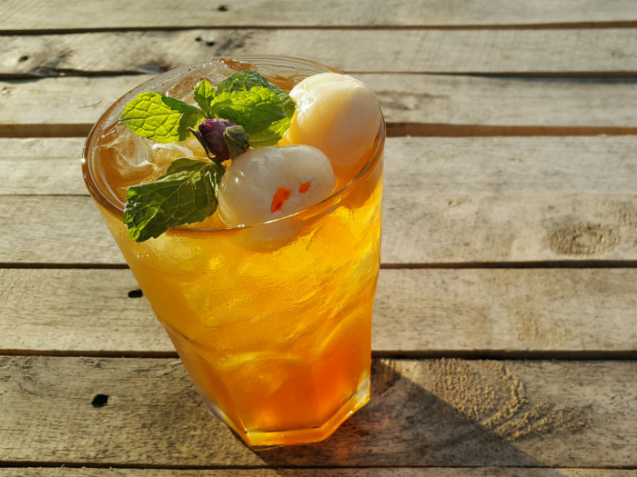 A glass of yellow-colored tea topped with mint and fruit, placed on a wooden platform