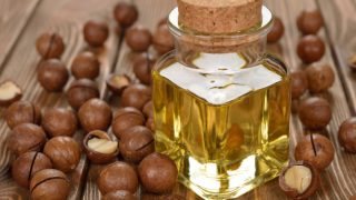A bottle of macadamia nut oil surrounded with macadamia nuts on a wooden table