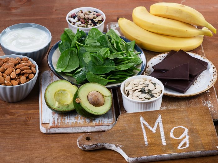 Magnesium-rich foods such as almonds, bananas, legumes, spinach, dark chocolate, and avocado on a wooden table