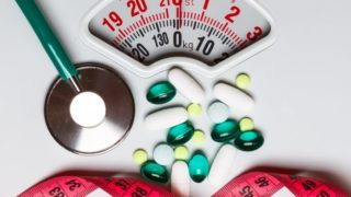 pills, stethoscope, and measuring tape on a weighing scale