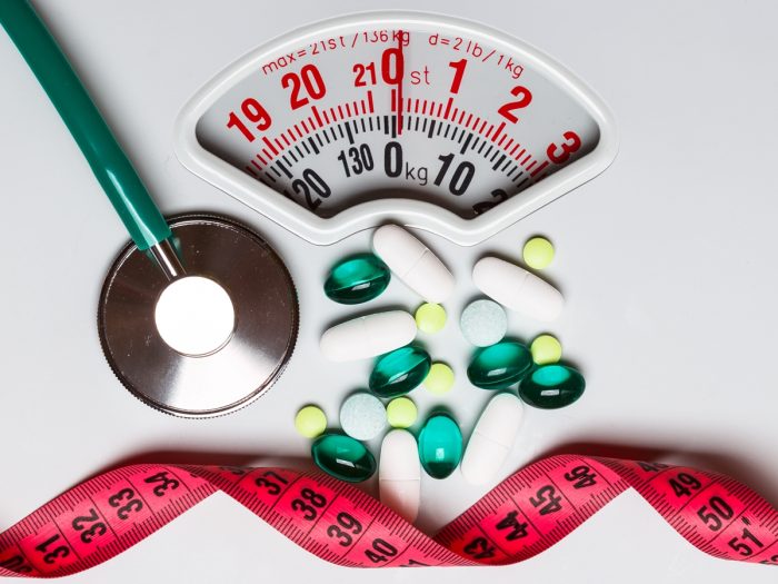 pills, stethoscope, and measuring tape on a weighing scale