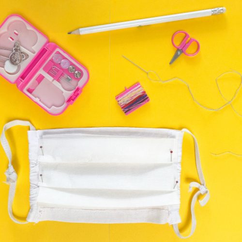 Top view of a homemade face mask with a sewing kit on a yellow background