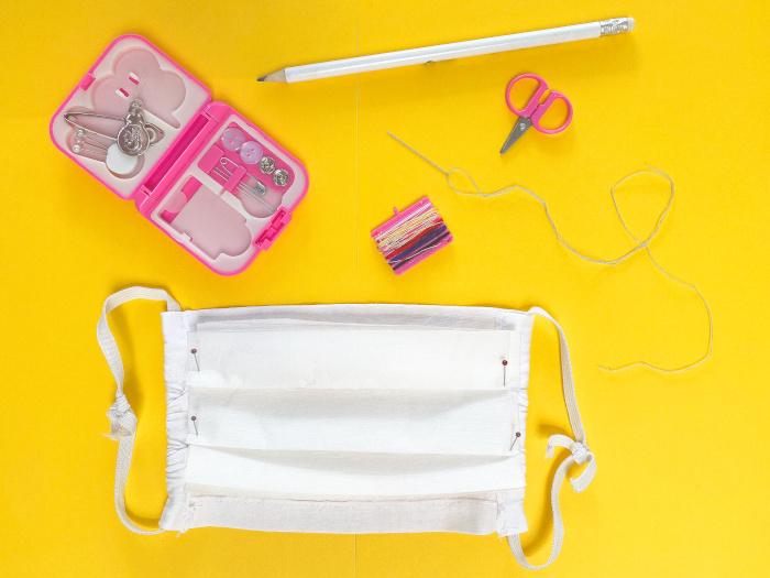 Top view of a homemade face mask with a sewing kit on a yellow background