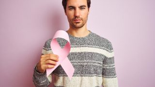 A man holding a pink cancer ribbon standing against a pink background