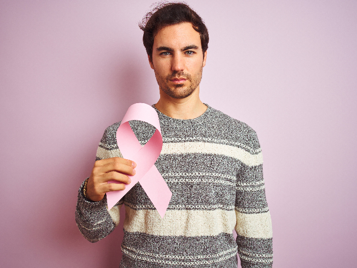 A man holding a pink cancer ribbon standing against a pink background