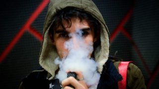 Young man's face partially covered in smoke from an e-cigarette