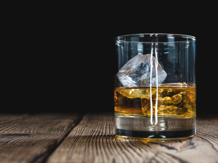 A glass with malt liquor and ice in it on a wooden table-top